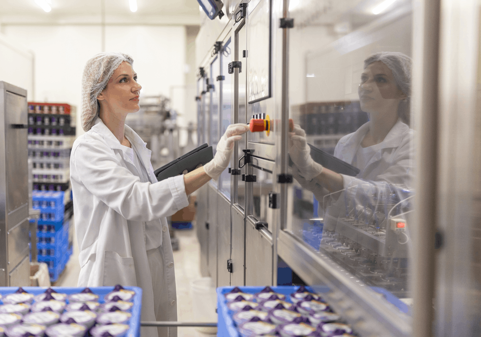 woman in a food production plant operating an automated control panel with packaged dairy containers in crates around her illustrating how modern manufacturers integrate old and new equipment systems and data sources for more stable efficient plant operations